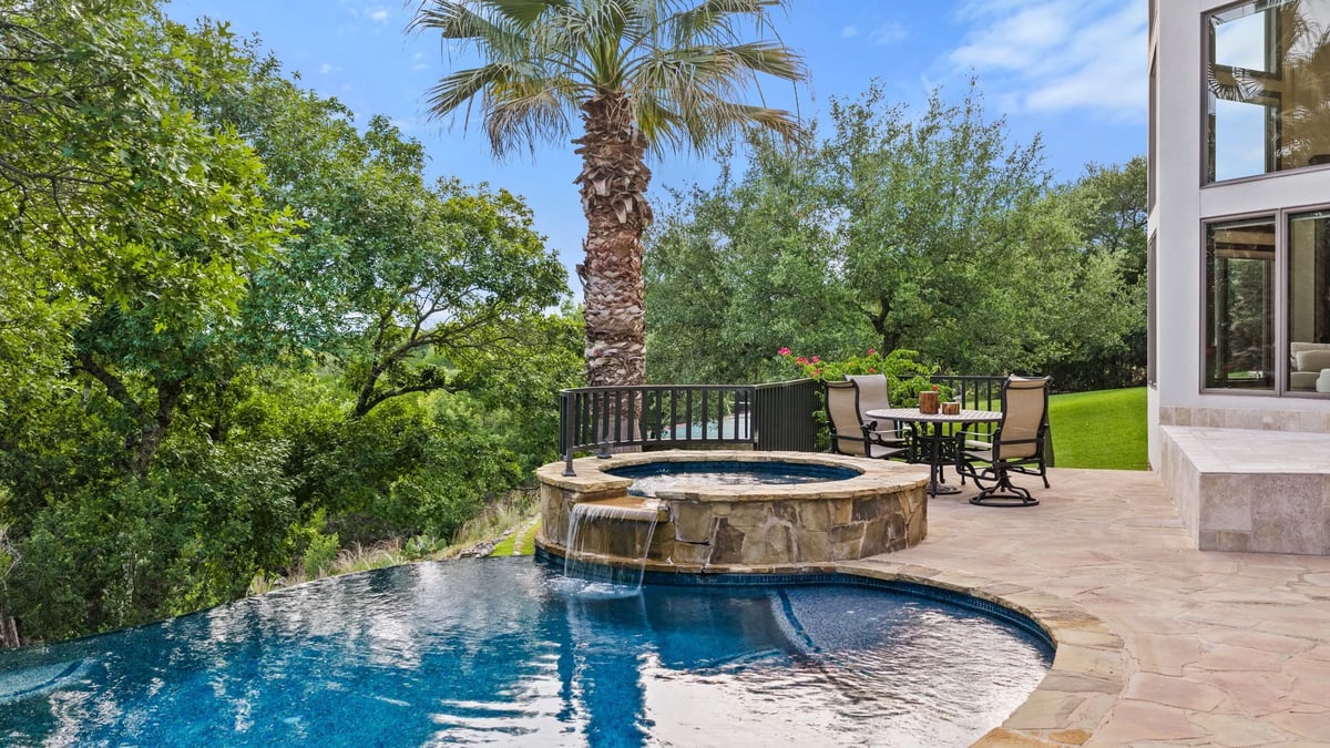 Negative-edge pool with raised stone hot tub and waterfall overlooking the wooded hillside