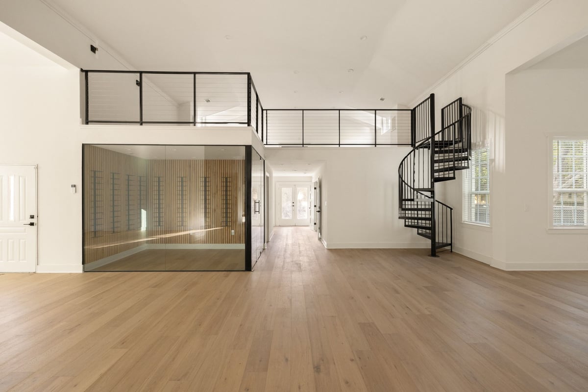 Living area with a glass-railed loft, a spiral stair and the glass-enclosed wine display