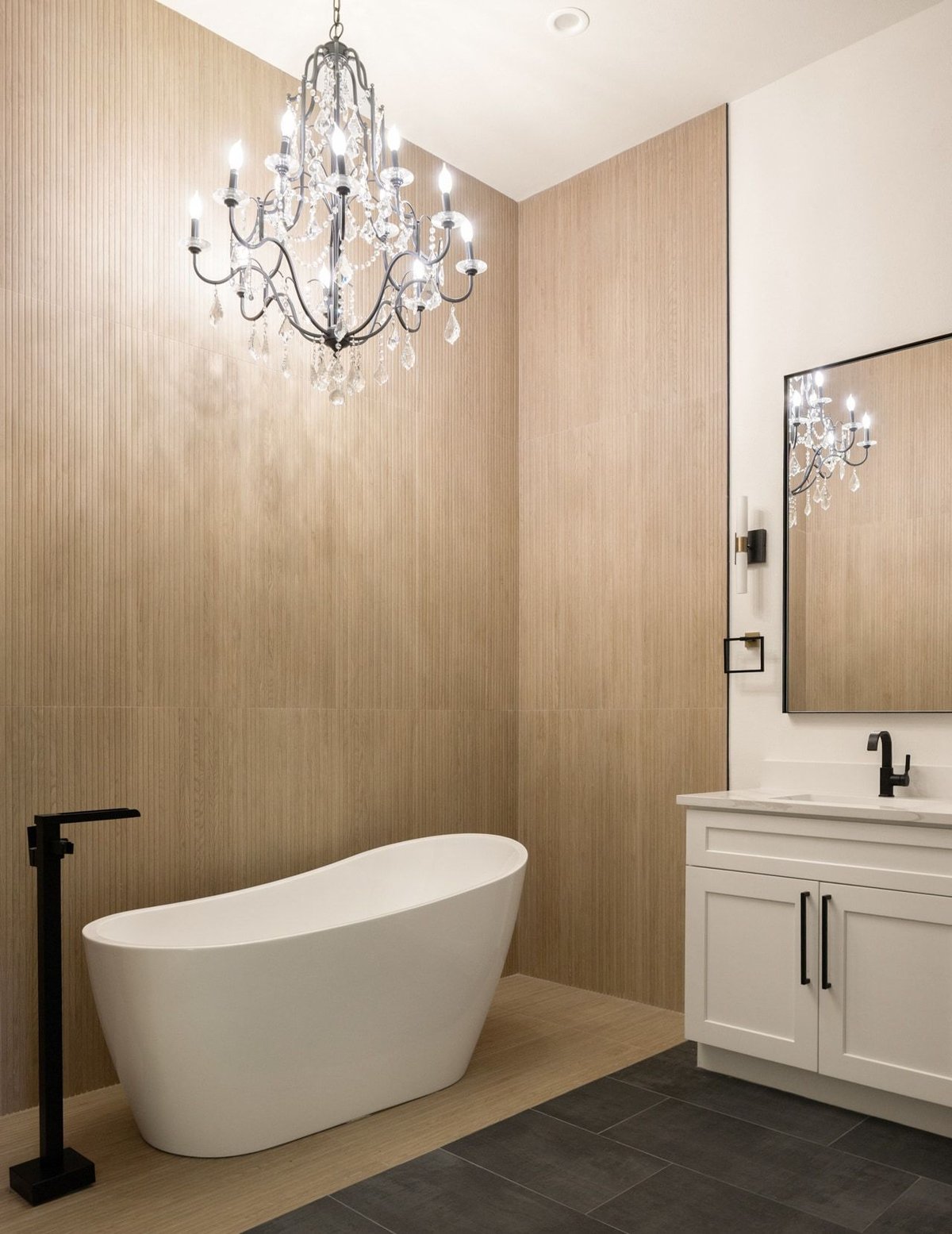 Freestanding soaking tub under a crystal chandelier beside a vanity