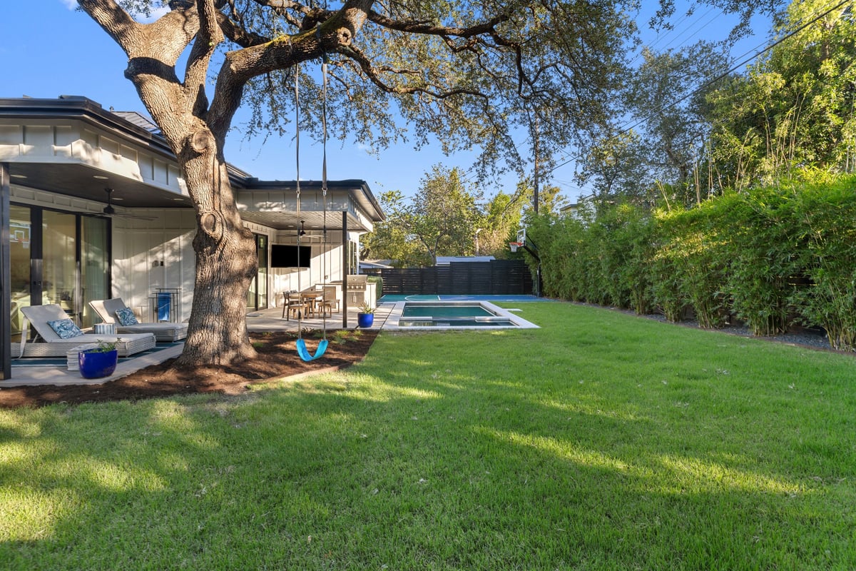 The backyard lawn under a large live oak with a rope swing, the covered patio at left and the pool beyond