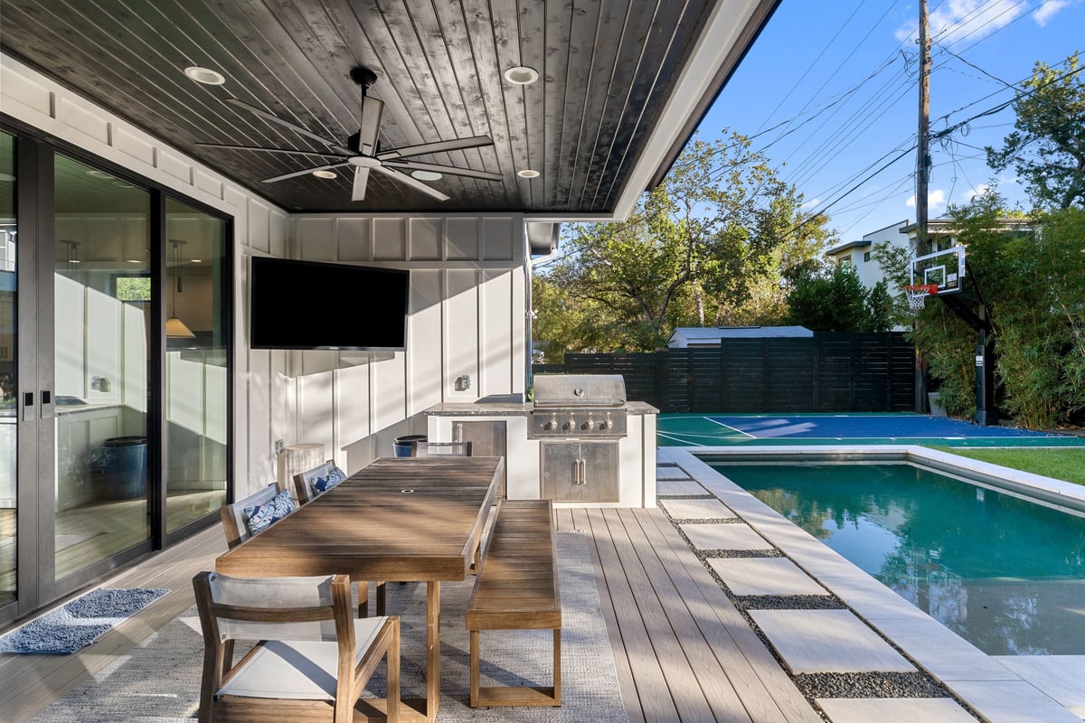 Covered patio with outdoor dining, a television and the outdoor kitchen beside the pool