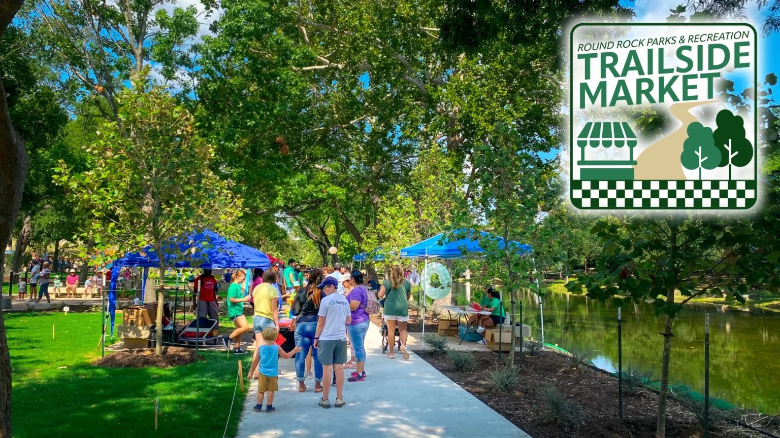 Outdoor market tents beneath trees beside a Trailside Market sign.