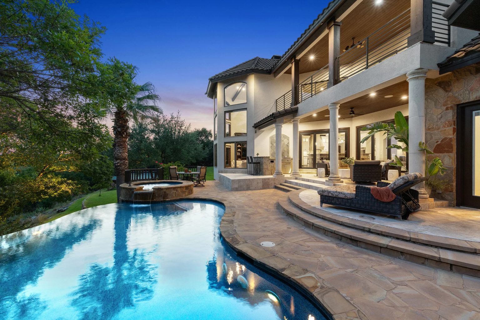 Twilight pool deck with a negative-edge pool, spa and covered two-story porch at a Keenan Group listing near Lake Georgetown