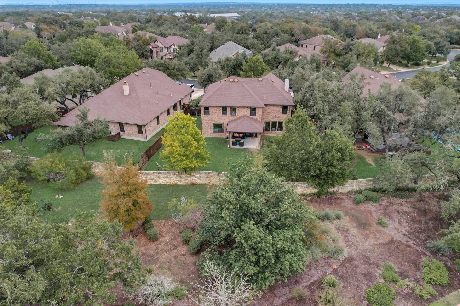 Aerial of brick two-story homes under live oaks backing onto a greenbelt in 78739, Austin