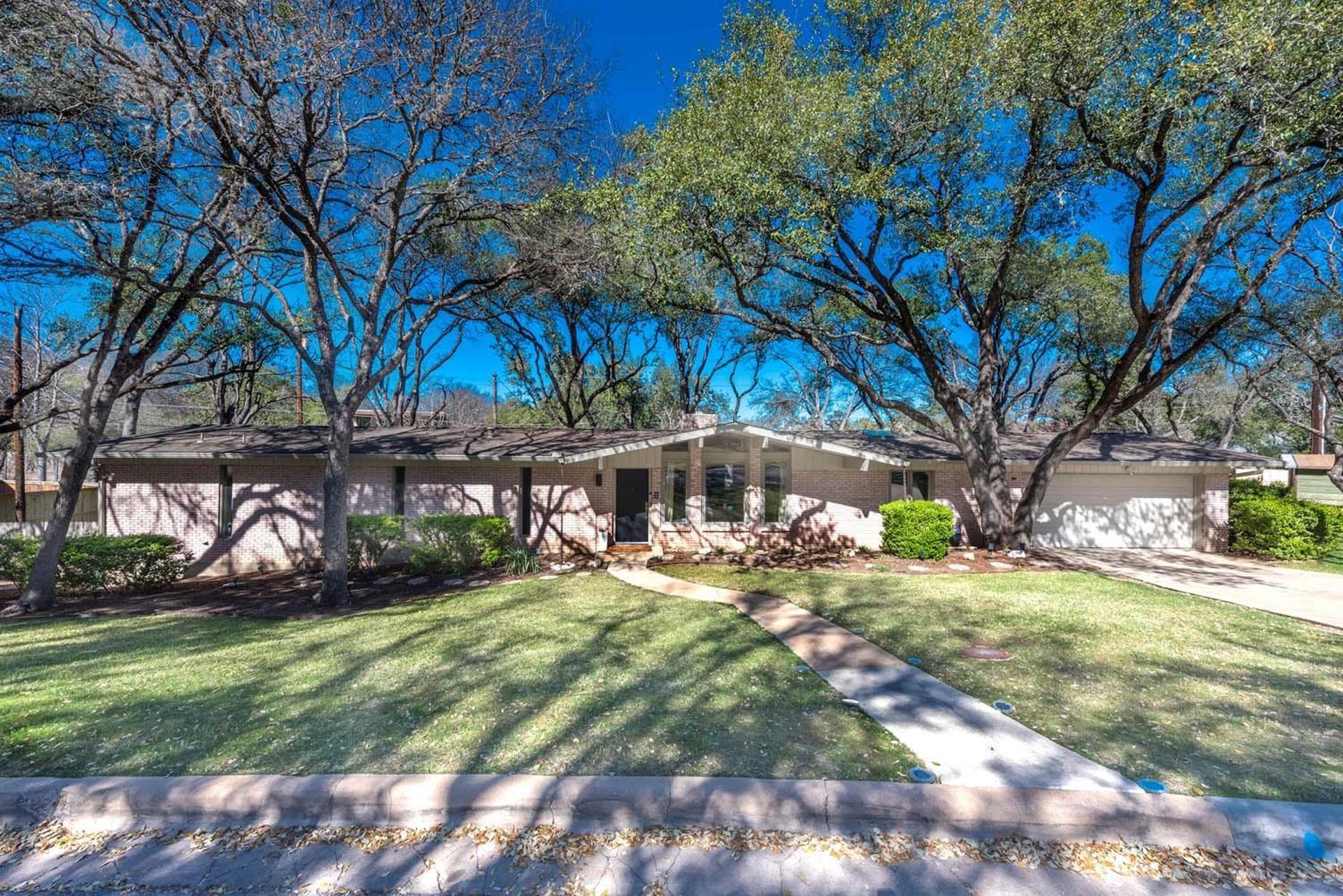 Single-story home under spreading live oaks, daytime, Austin