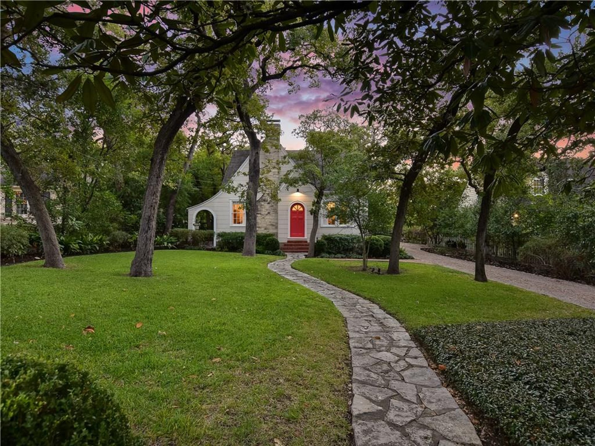Tudor-style cottage with red door, stone path and lawn at dusk, Austin