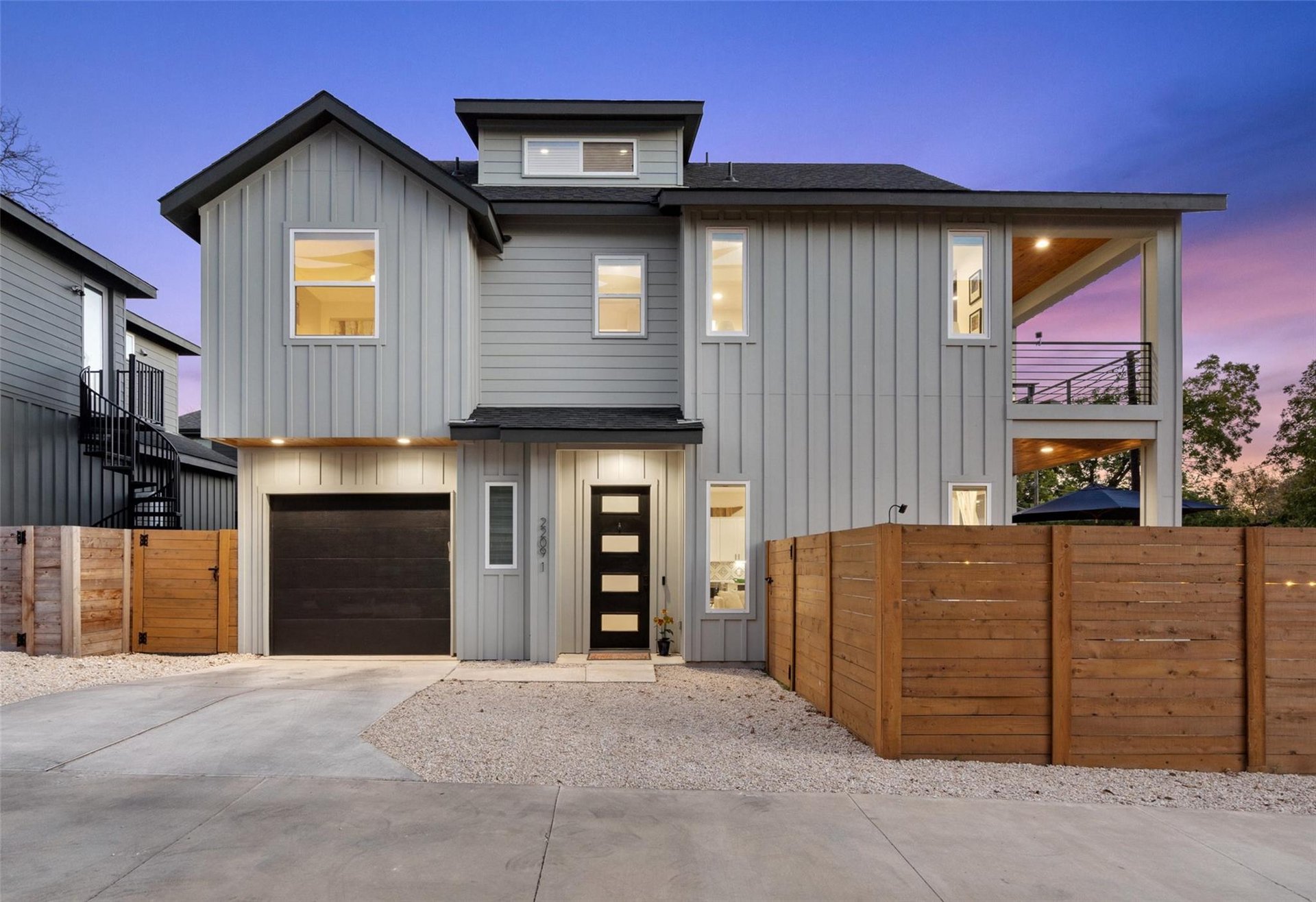 Gray modern two-story home with a garage and wood fence at dusk in 78722, Austin