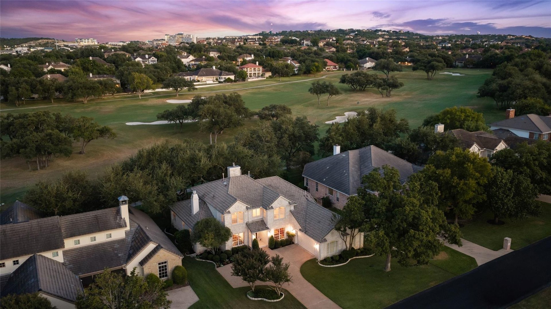 Aerial of a two-story home beside a golf course with Hill Country beyond, dusk, The Hills