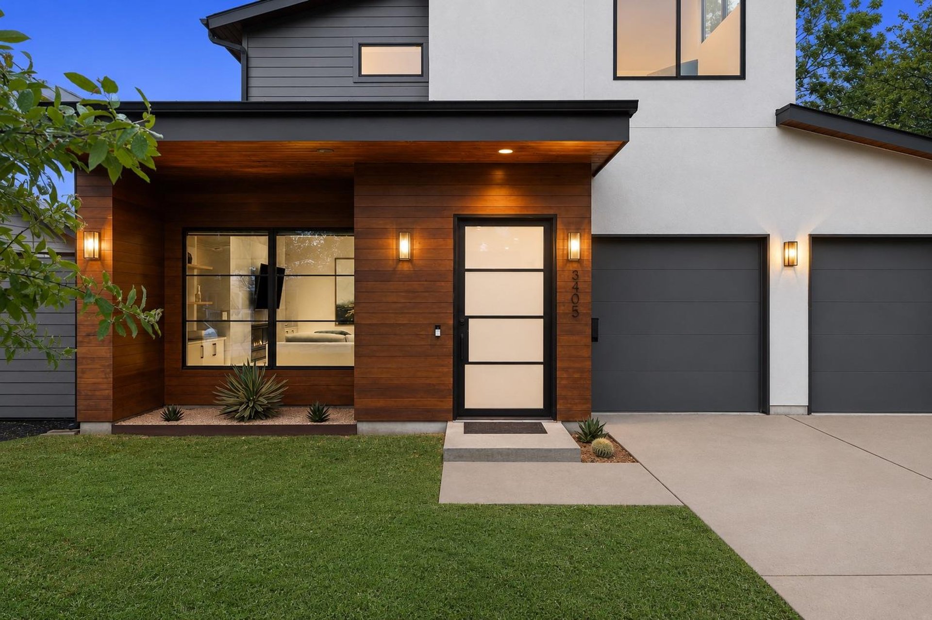 Modern home entry with wood-clad porch and dark garage doors at dusk, Austin