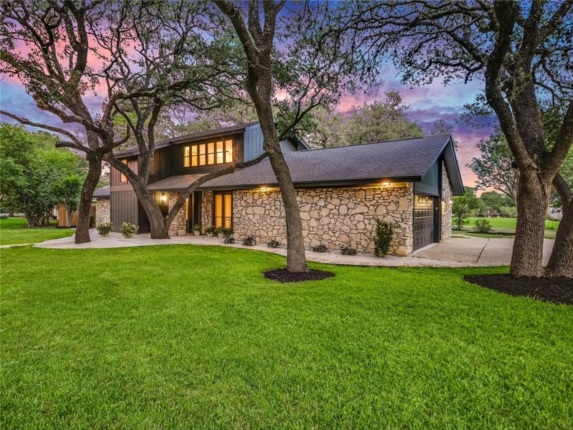 Stone and dark-sided home under live oaks at sunset, Austin