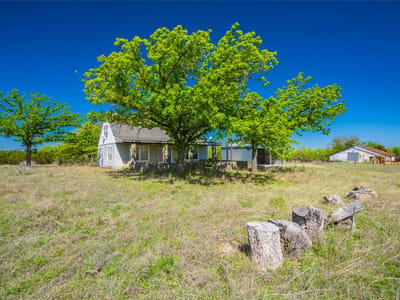 Front exterior with small ranch house and large shade tree at 0 County Road 208 - Watson, TX