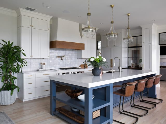 White kitchen with a blue island and brass pendants at 7218 Valburn Drive, Austin